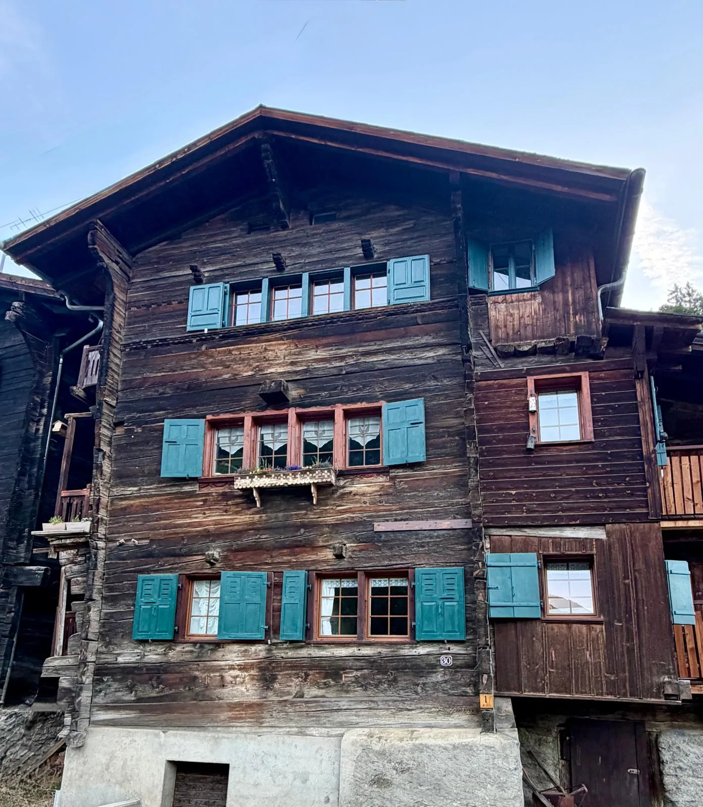La maison WHAT, un chalet valaisan en bois aux volets verts, à Mâche